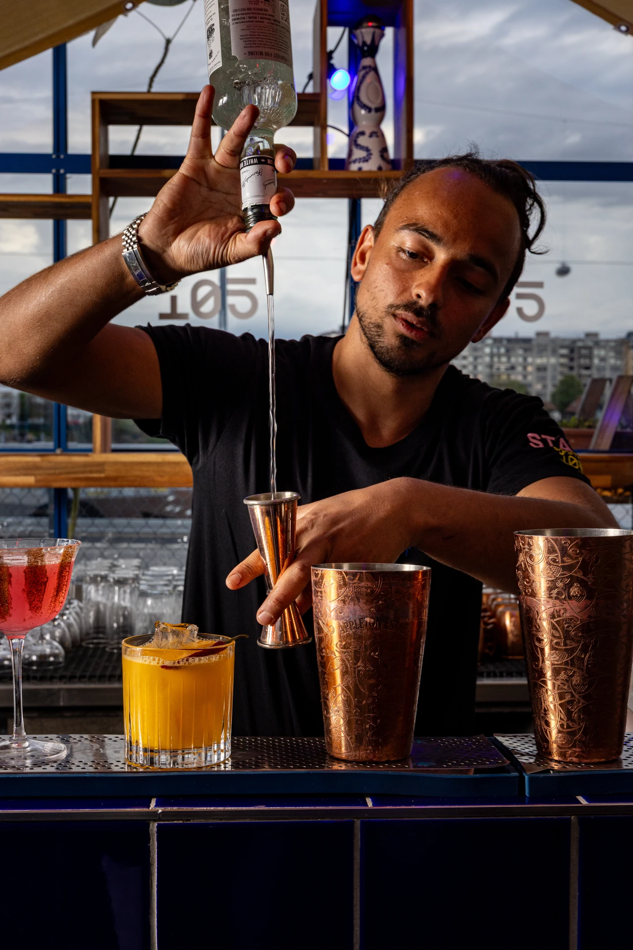 Barman versant un rhum blanc dans un jigger en cuivre derrière le bar