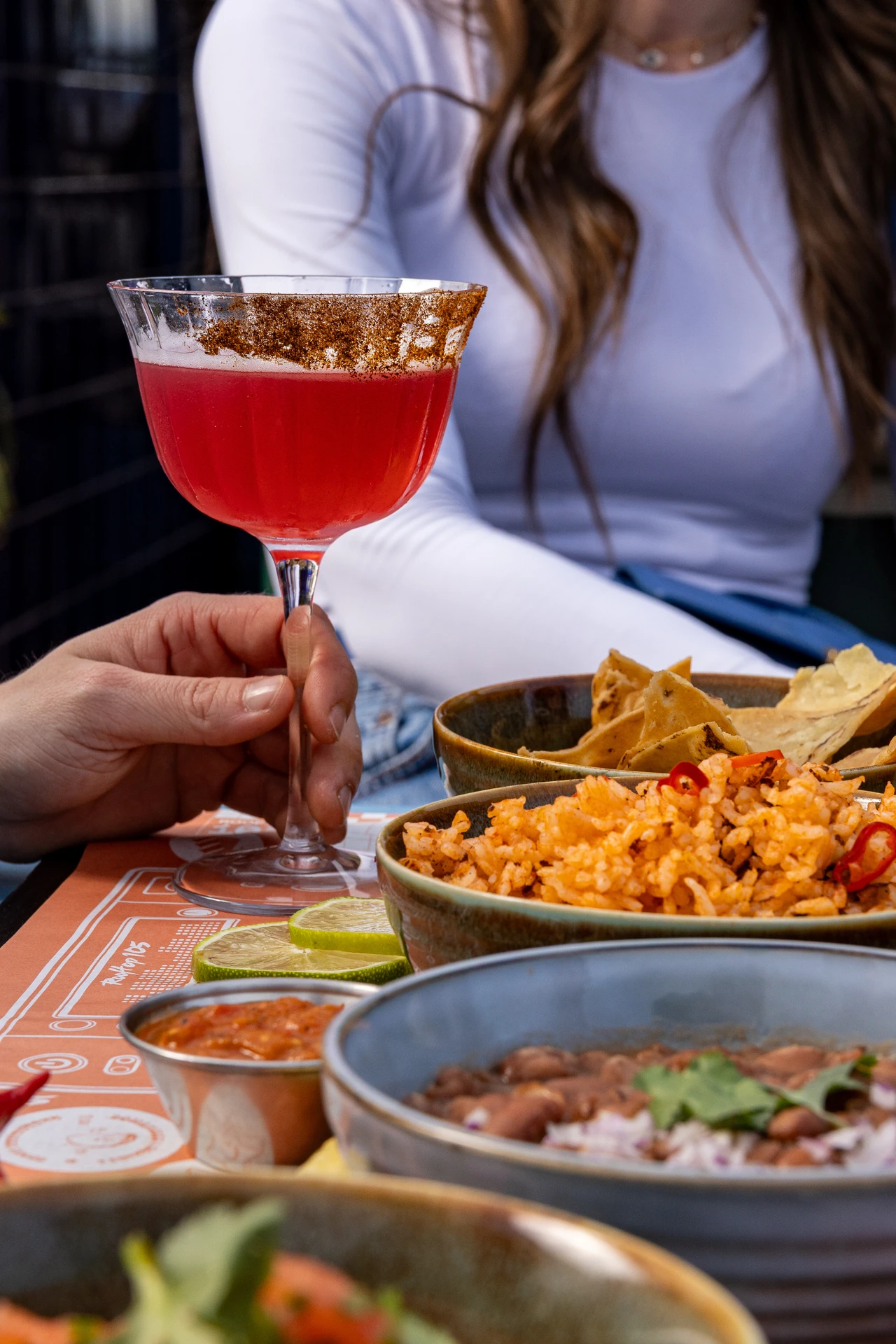 Cliente tenant un cocktail rouge devant un feast mexicain partagé en terrasse