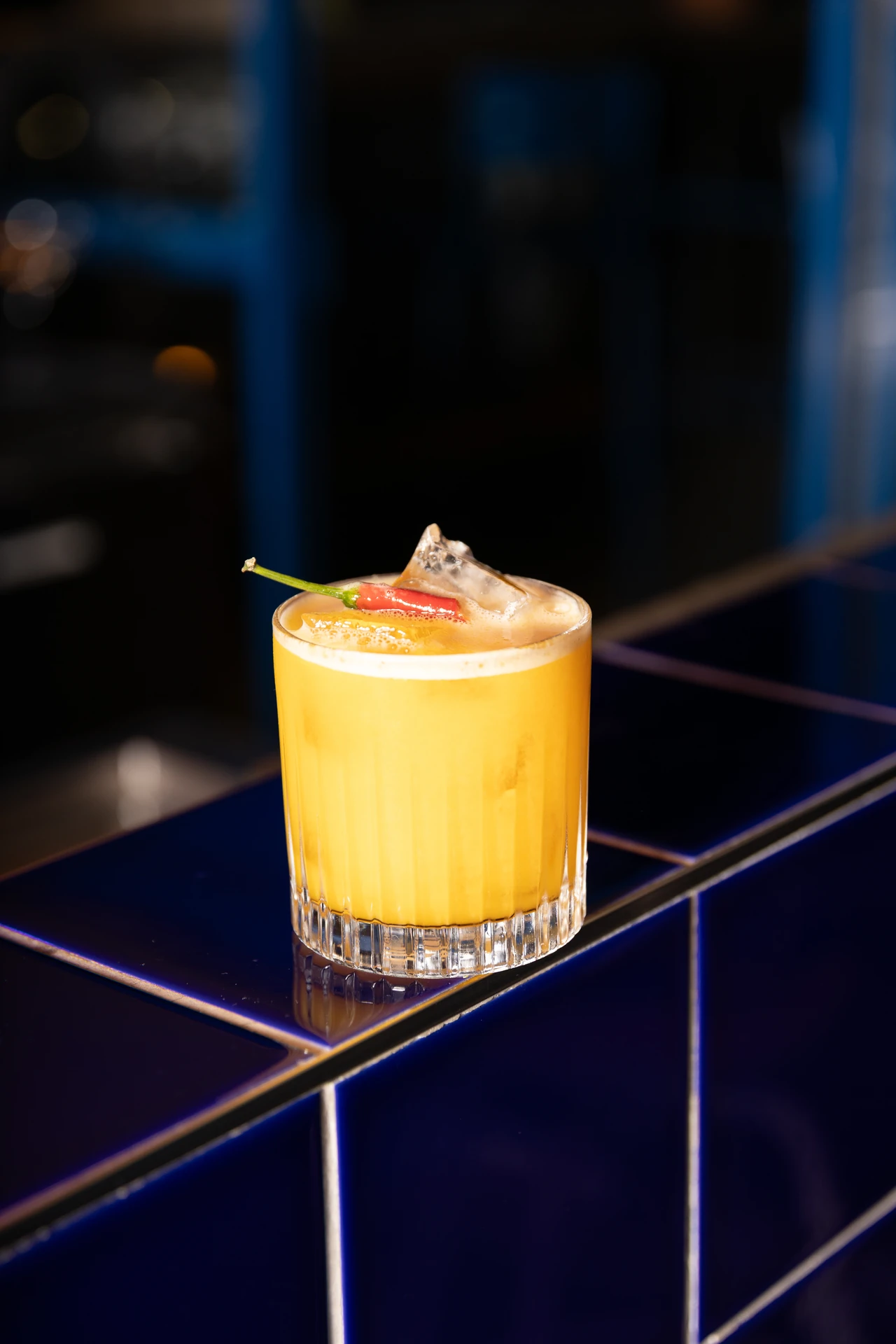 Cocktail signature mangue et piment posé sur le bar carrelé bleu nuit