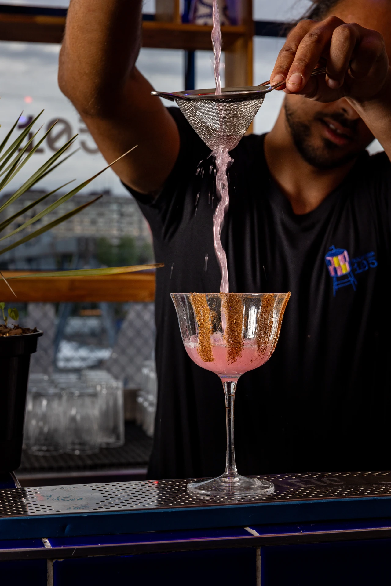Cocktail rose versé à la passoire dans une coupe givrée d'épices au Rooftop 105