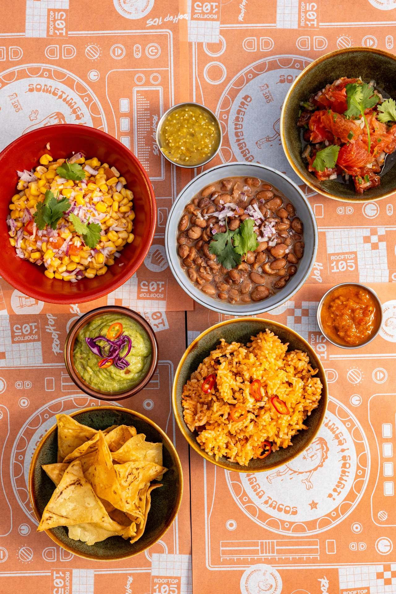 Sides mexicains sur set de table orange: maïs, haricots, riz, guacamole, salsas